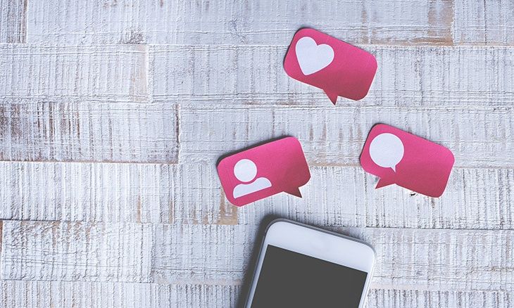 Photo d'un smartphone et d'exemples de réaction sur les réseaux sociaux (Like, Commentaire, Partage) sur une table.